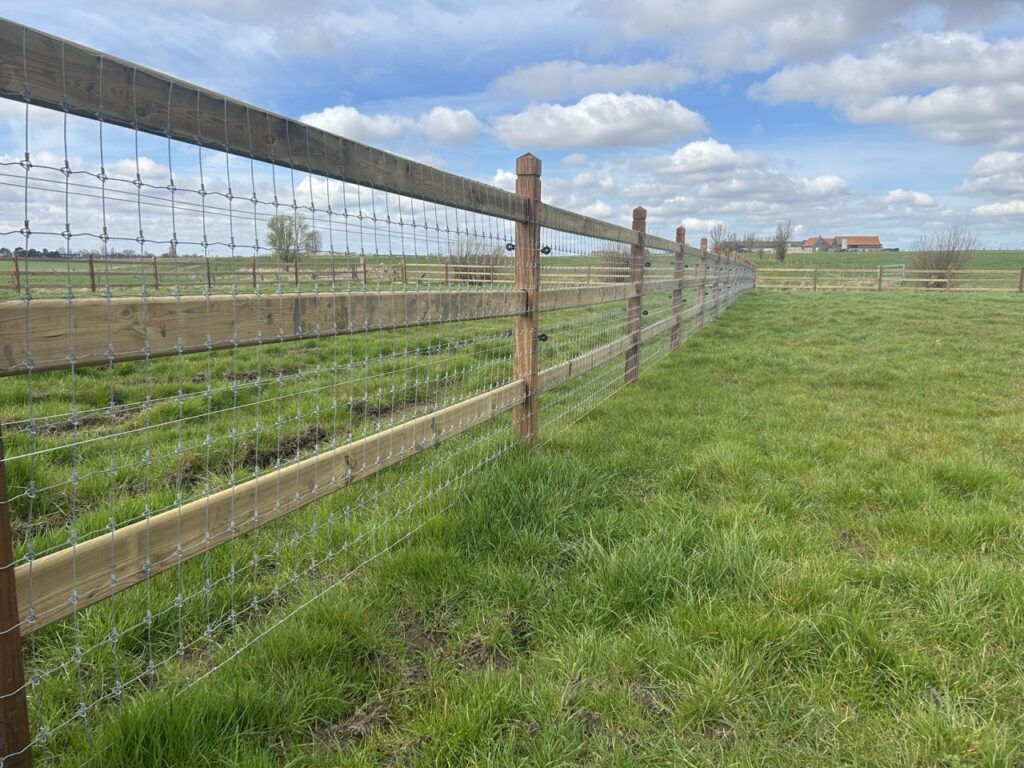 Draadnet omheining met houten palen en latten op een groene weide voor dierenafbakening