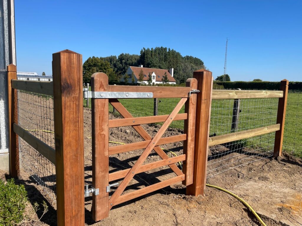 houten poort met gaasomheining voor dierenafbakening op boerenland onder blauwe hemel