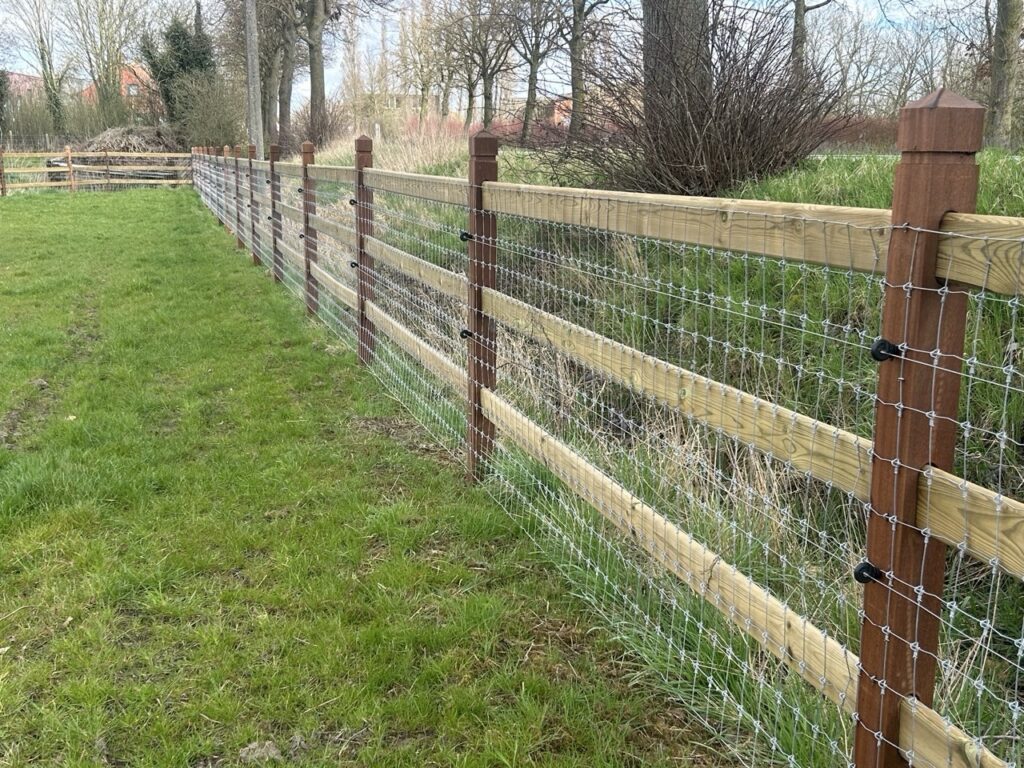 Draadgaas omheining met houten liggers en palen als afbakening voor dieren op een groene grasweide
