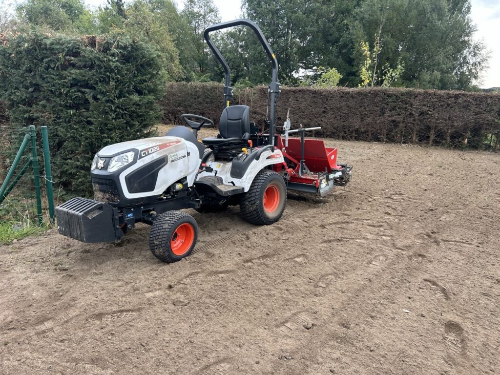 tuintractor met grondbewerkingstoestel op omheind weiland met heggen en dierenafbakening