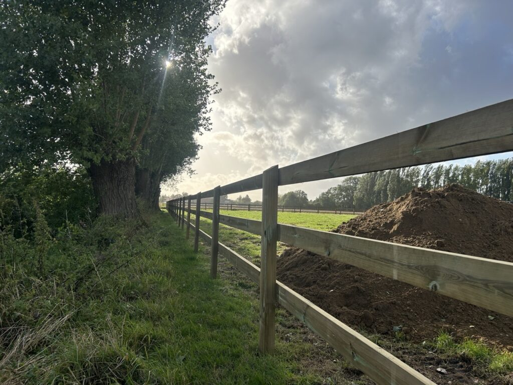 houten perceelafscheiding met drie planken langs grasveld en bomen in zonlicht