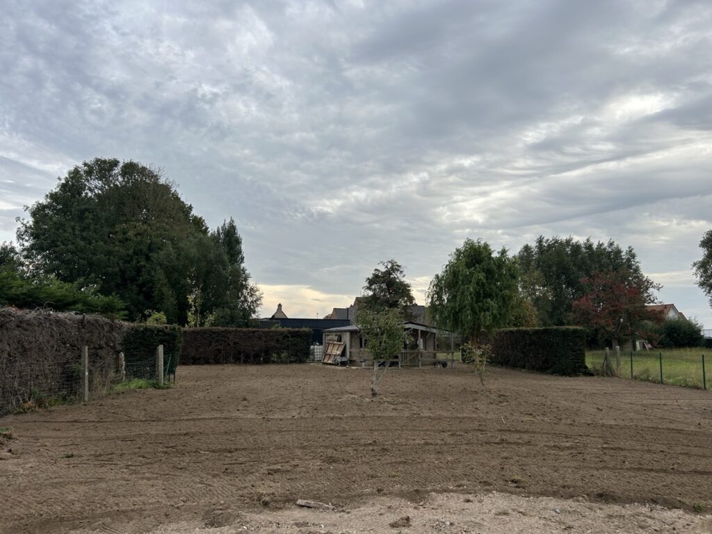 omheining met draad en houten palen rond een afgezet stuk grond met bomen en een schuur op de achtergrond