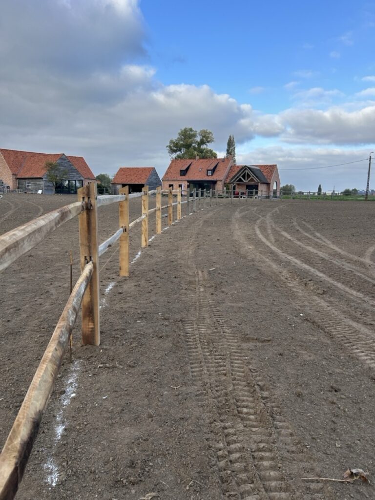 Houten omheining langs een landbouwveld met traditionele boerderijen op de achtergrond