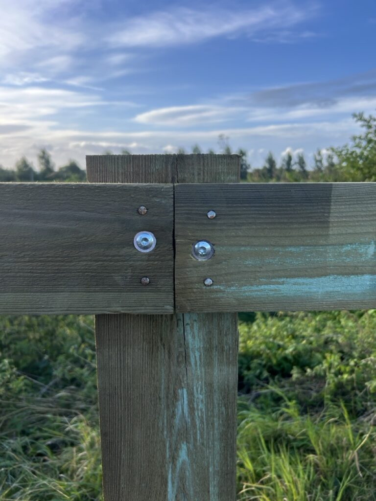 Houten afrastering bevestigd met metalen schroeven in groene natuuromgeving bij Nieuwlandzicht