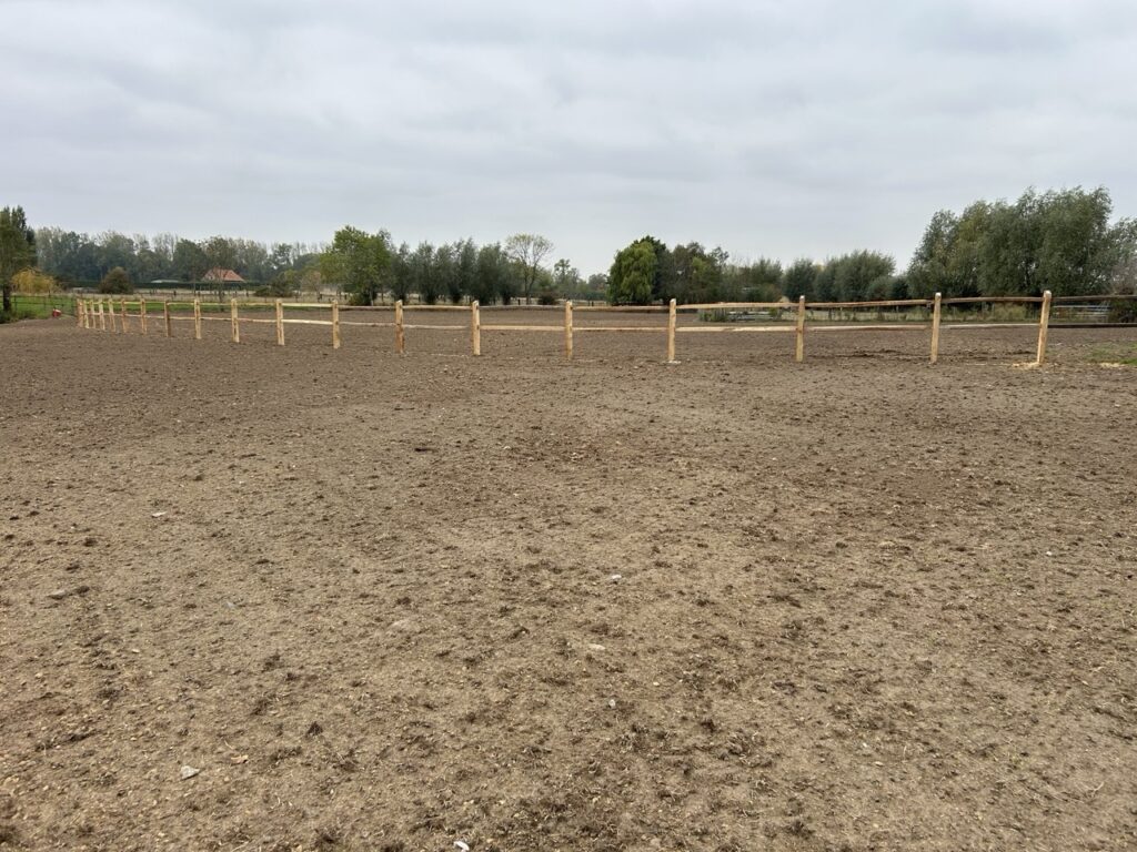 houten omheining met twee horizontale latten op een ruime paardenpaddock onder bewolkte hemel