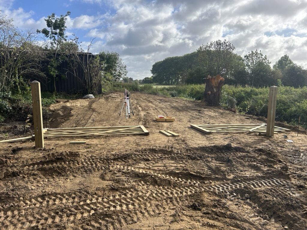 Beginnende installatie van een houten afrastering met palen en poorten op een bouwterrein met landbouwgrond op de achtergrond